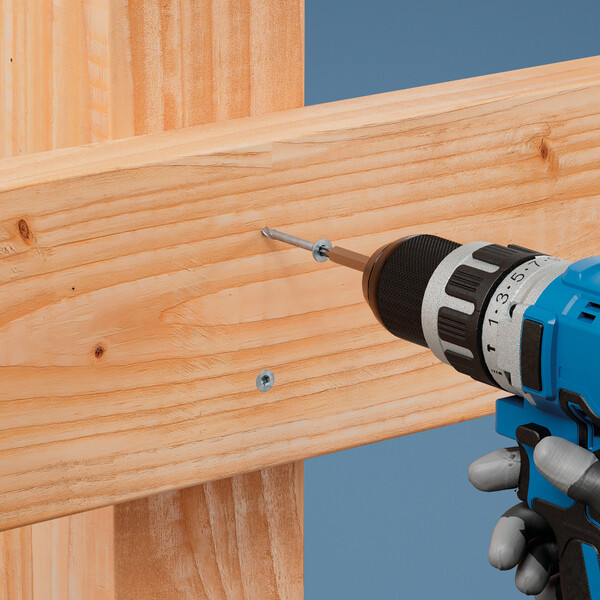 Ein motorisierter Schrauber in Blau von rechts, der eine Schraube in ein hölzernes Brett eindreht. Ein weiteres Stück Holz hält das Brett auf der hinteren Seite, eine Schraube ist bereits eingedreht. Der Hintergrund ist blau. Die Hand, die den Schrauber hält, ist teilweise sichtbar und steckt in einem grauen Handschuh.