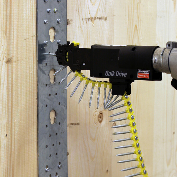 Ein Quik Drive-Vorsatz an einem motorisierten Schrauber, geladen mit einem Streifen magazinierter Schrauben. Mit einer davon dreh er gerade eine Schraube in einen Zuganker an einer hölzernen Wand ein.