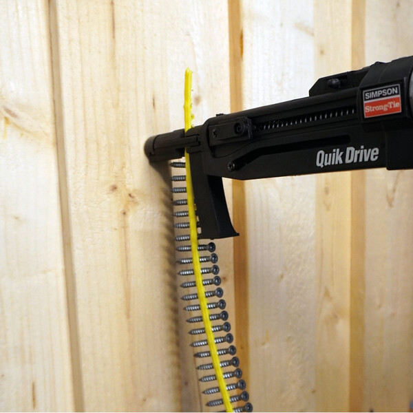 Ein Quik Drive-Vorsatz, von rechts kommend und mit einem Streifen magazinierter Schrauben ausgestattet. Eine Schraube wird in eine hölzerne Wand eingeschraubt.