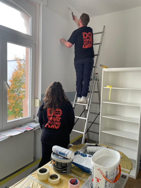 Zwei Menschen stehen vor Wand. Einer streicht.