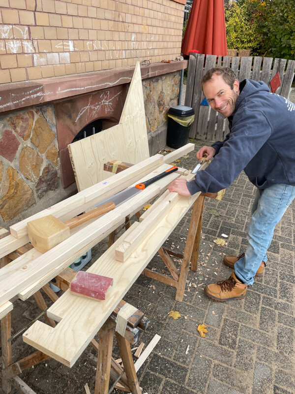 Mann grinst in die Kamera und schraubt an Holz herum.