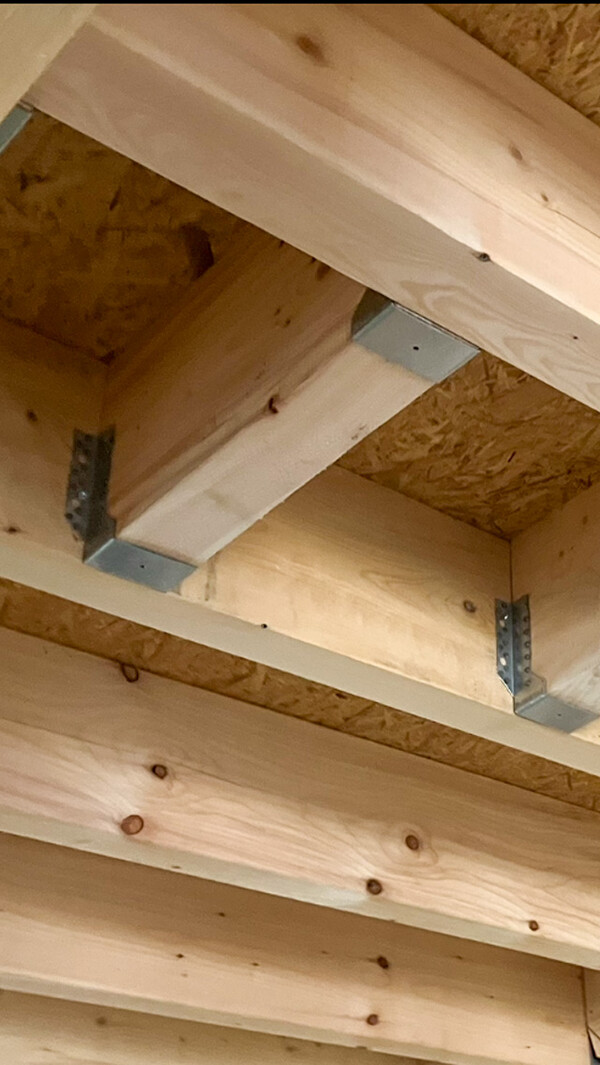 Eine Holzkonstruktion: Hölzerne Balken tragen eine hölzerne Decke. Die quer verlaufenden Balken sind mit Balkenschuhen von Simpson Strong-Tie befestigt, mit BSNN.