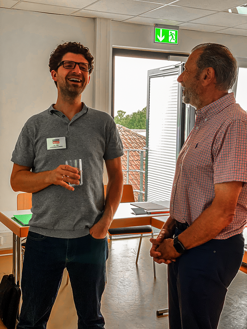 Dr.-Ing. Johannes Hummel lachend im Gespräch mit einem der Akademieteilnehmer.