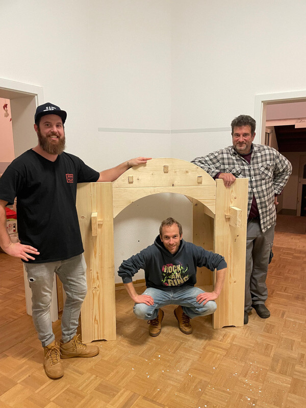 Drei Menschen stehen um und in einer Holzkonstruktion.